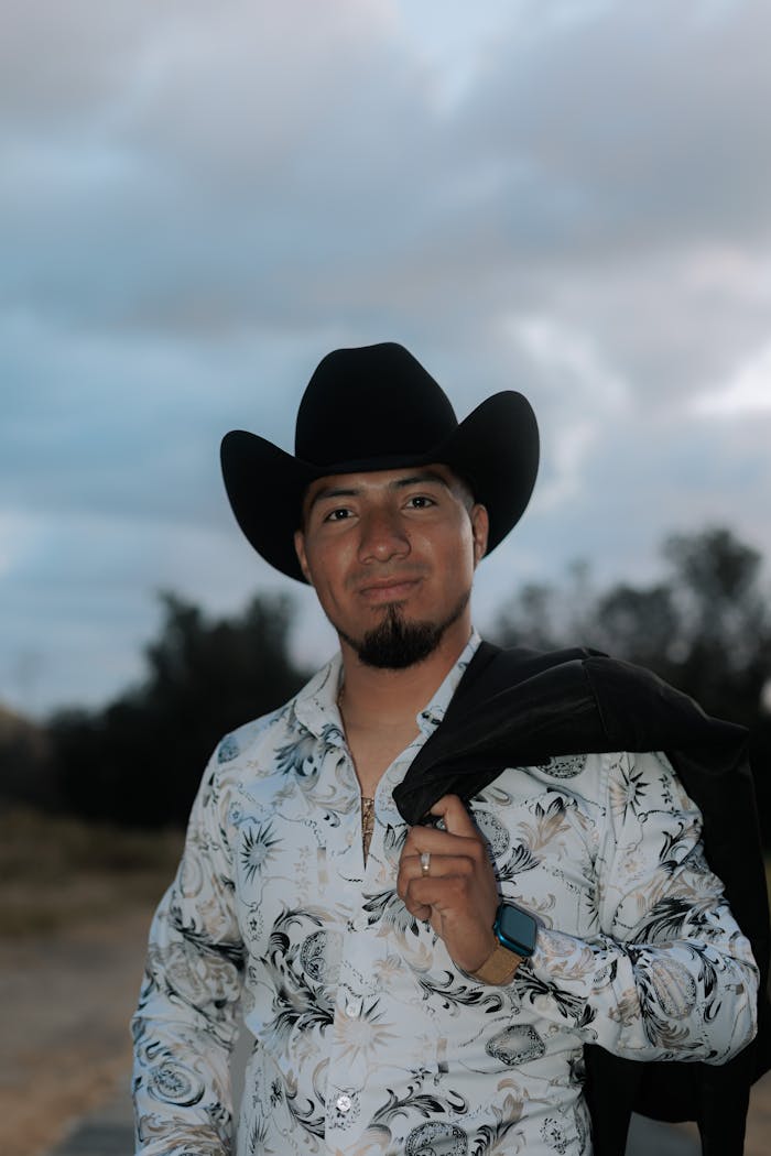 Portrait of a man in a cowboy hat standing outdoors against a twilight sky, exuding confidence and style.